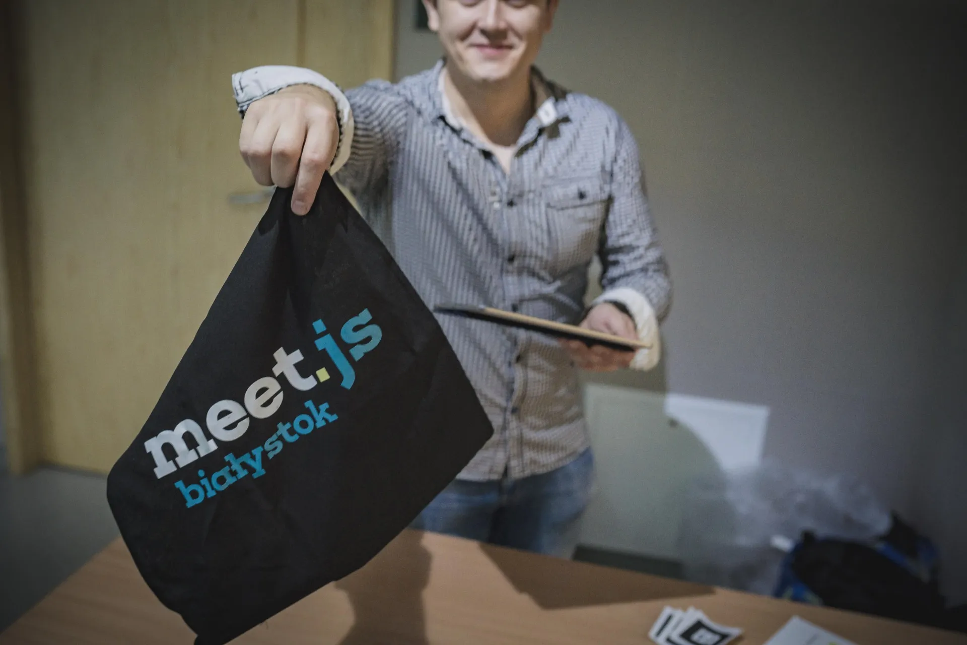 Smiling man holding a black meet.js Białystok tote bag out towards the camera