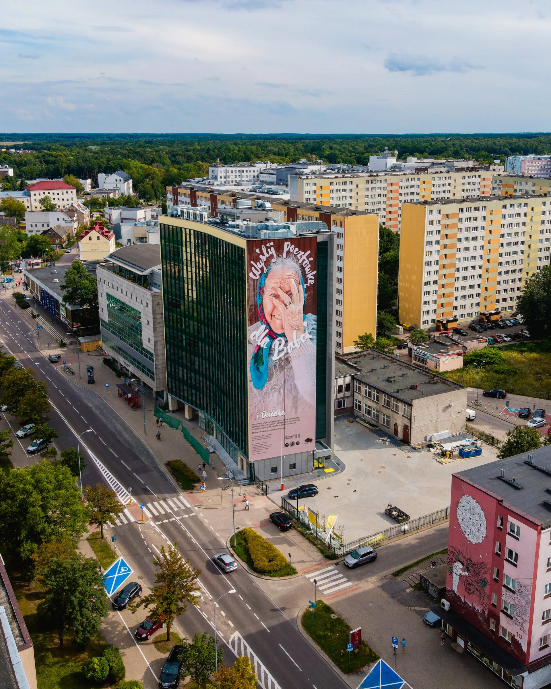 Drone view of a high-rise on Skłodowskiej-Curie Street in Białystok with a mural of Grandma Eugenia and the words “Wyślij pocztówkę dla Babci”
